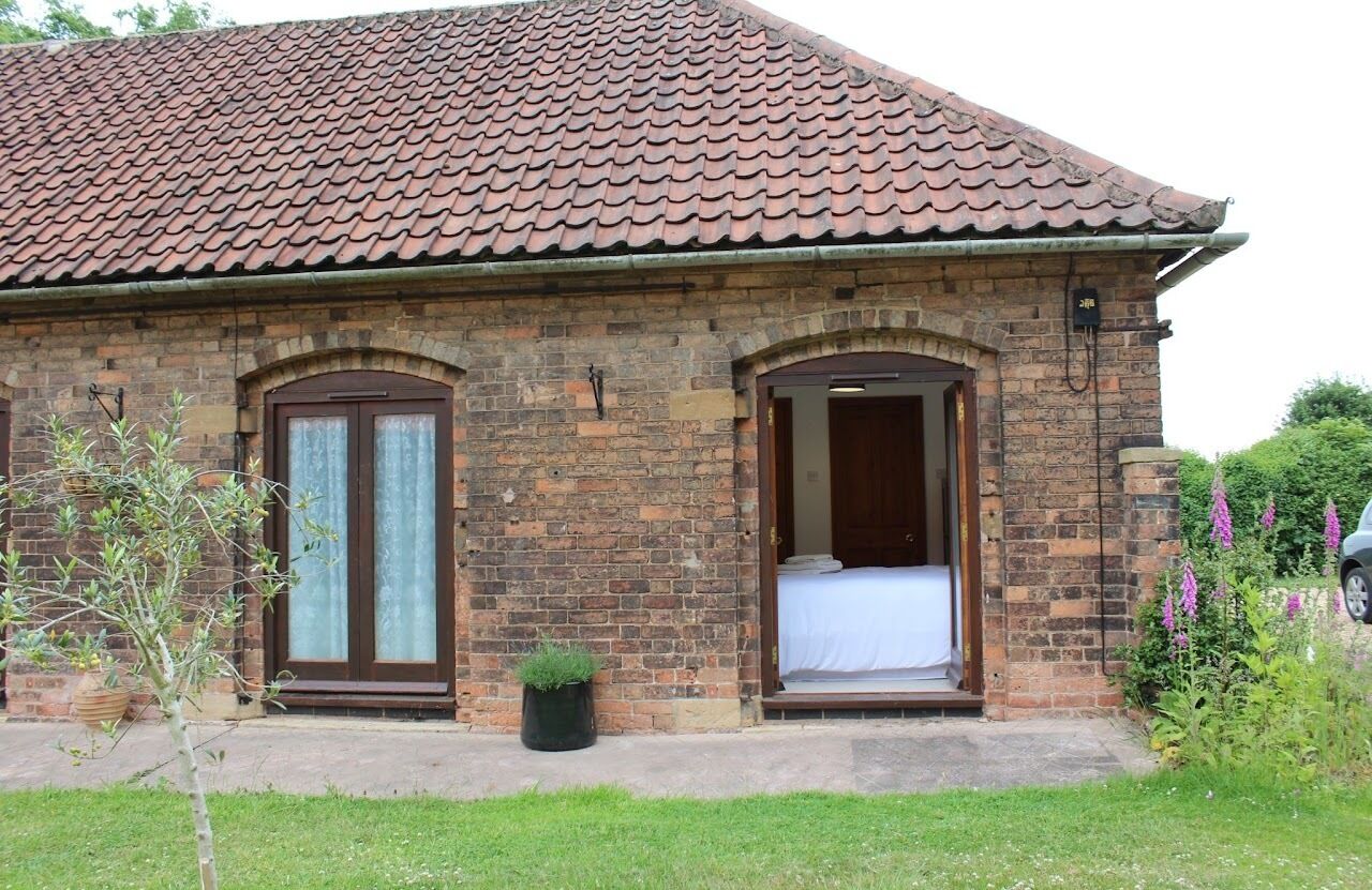 A brick building with a tiled roof, two arched doorways, and a small garden area with a potted plant.