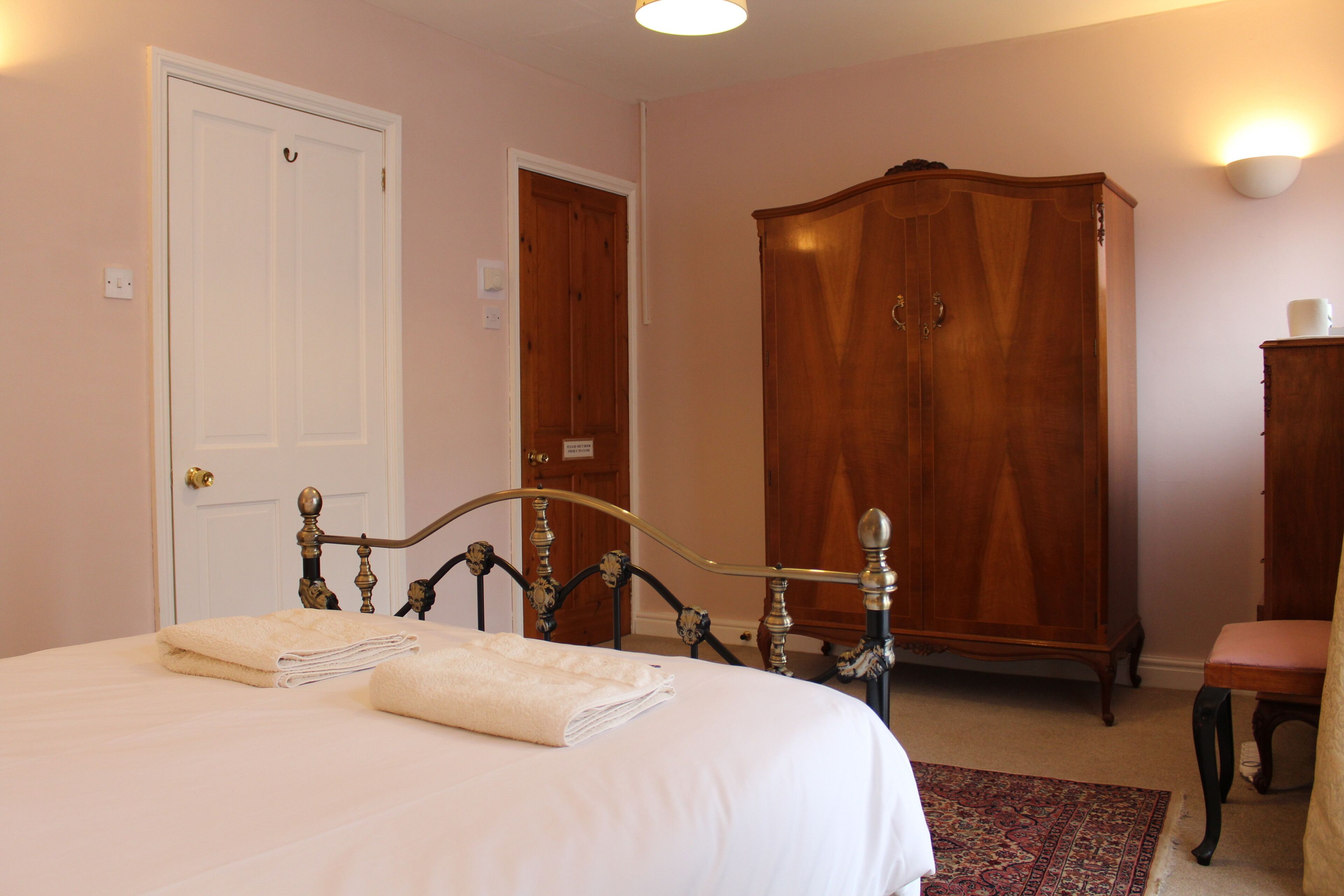 A bedroom with a bed, a wardrobe, a chair, and a carpeted floor.