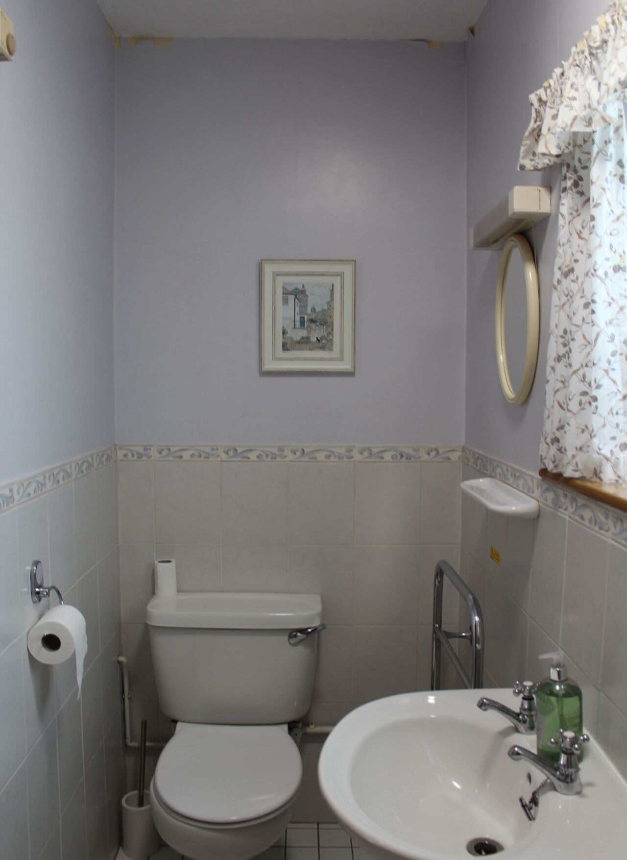 A bathroom with a toilet, sink, and a framed picture on the wall.
