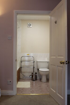 A narrow bathroom with a toilet, a towel rack, and a trash can.