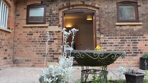 Un bâtiment en briques avec une porte, des fenêtres et un banc en métal agrémenté de plantes.