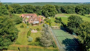 Un vaste domaine comprenant une maison principale, un court de tennis et des jardins environnants.