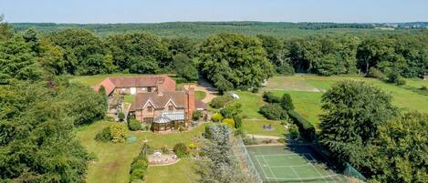 A large estate with a main house, tennis court, and surrounding gardens.