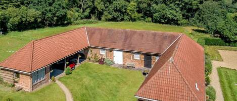 A large, L-shaped brick building with a red-tiled roof, a covered garage, and a well-maintained lawn.