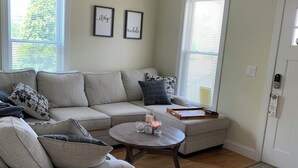 Ein Wohnzimmer mit einem Ecksofa, einem runden Couchtisch und zwei gerahmten Schildern an der Wand.
