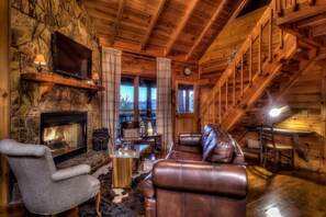 A cozy log cabin interior with a stone fireplace, leather furniture, and a television mounted on the wall. - Recently Renovated|Pet-Friendly|Mtn Views|Hot Tub (Blue Ridge)