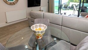 A modern living room with a sofa, a glass coffee table, a flat-screen TV, and a view of the outdoors. - Peninsula Apartment 2 (St Ives)