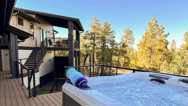 A hot tub on a wooden deck with a view of trees and a building in the background. - Carriage House (Show Low)