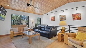 A spacious living room with a wooden ceiling, large windows, and a black leather sofa. - Carriage House (Show Low)