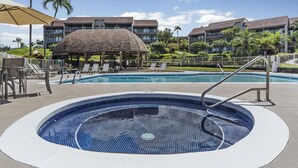 Un espace piscine doté de chaises longues et d’un jacuzzi, entouré d’un bâtiment à toit de tuiles et de palmiers.