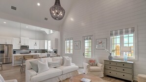 A spacious living room with a white sofa, a wooden coffee table, and a dining area with a kitchen in the background.