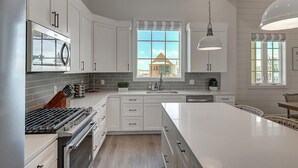 A modern kitchen with white cabinetry, a large island, and a view of a house through the windows.