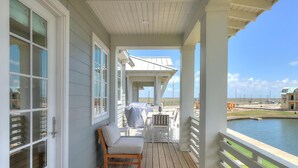 A covered porch with a wooden bench and a table, overlooking a body of water and a distant building.