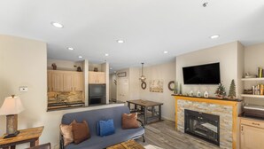 A modern living room with a sofa, fireplace, television, and kitchen in the background. - Patio access to Keystone Lake & Gorgeous Views, Easy Access to Everything! (Keystone)