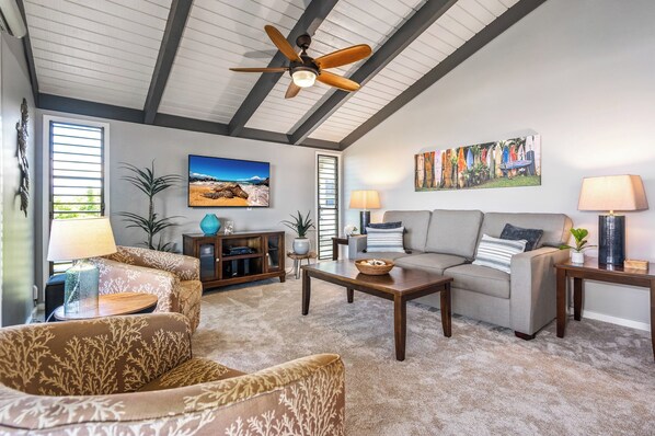 A spacious living room with a ceiling fan, a large painting, a sofa, a coffee table, and a TV.