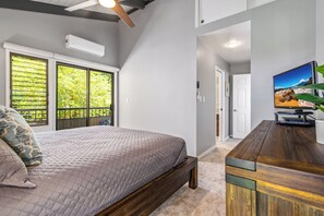 A bedroom with a bed, a wooden desk, a television, and a window with blinds.