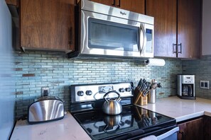 A kitchen with a stainless steel microwave, a stove with a kettle, and a toaster.