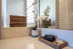 A bathroom with a wicker basket, a potted plant, a tray with a towel and toiletries.