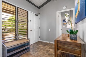 A room with a wooden bench, a small table with a plant, and a door with a view of greenery outside.
