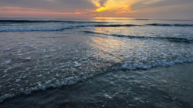 Une plage avec des vagues et un coucher de soleil.