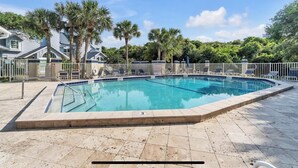 Une piscine rectangulaire bordée de carreaux, entourée de palmiers et d’une clôture blanche.