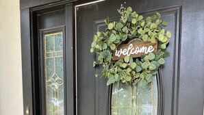 A black door with a 'welcome' sign and a green wreath. - Sunrose Cottage - Fresh & Clean - King Suite + free Wifi - Pet Friendly (Cibolo)