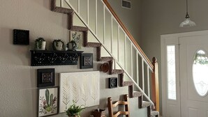 A staircase with a wooden handrail and a white railing, leading to a landing with a round table and a chair. - Sunrose Cottage - Fresh & Clean - King Suite + free Wifi - Pet Friendly (Cibolo)