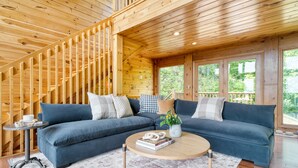 A wooden interior with a blue sofa, a round coffee table, and a staircase.