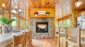 A wooden interior with a stone fireplace, wooden dining table, chairs, and a refrigerator.