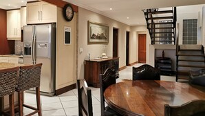 Una cucina moderna con elettrodomestici in acciaio inossidabile, un'area pranzo con tavolo e sedie in legno, e una scala con ringhiera in vetro.