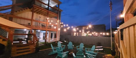 A two-story building with a balcony, outdoor seating area with chairs, and string lights.