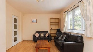 Una sala de estar con una mesa de centro de madera, dos sofás negros, un mueble de madera pequeño y un ventanal con cortinas.