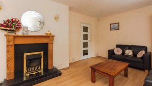 Una sala de estar con chimenea, un sofá de cuero negro, una mesa de centro de madera y una araña.