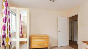 Un dormitorio con cama, armario con puertas espejadas, cómoda y puerta que da a otra habitación.