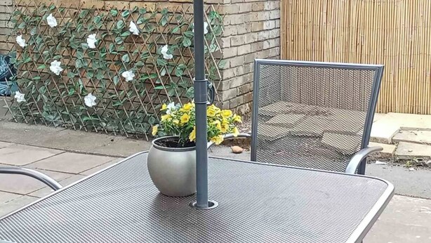 Juego de mesa y silla metálicos al aire libre, con una planta en maceta y una cerca al fondo.