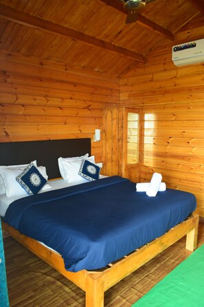 Ein Zimmer einer Holzhütte mit einem Bett, Kissen und einem Deckenventilator.