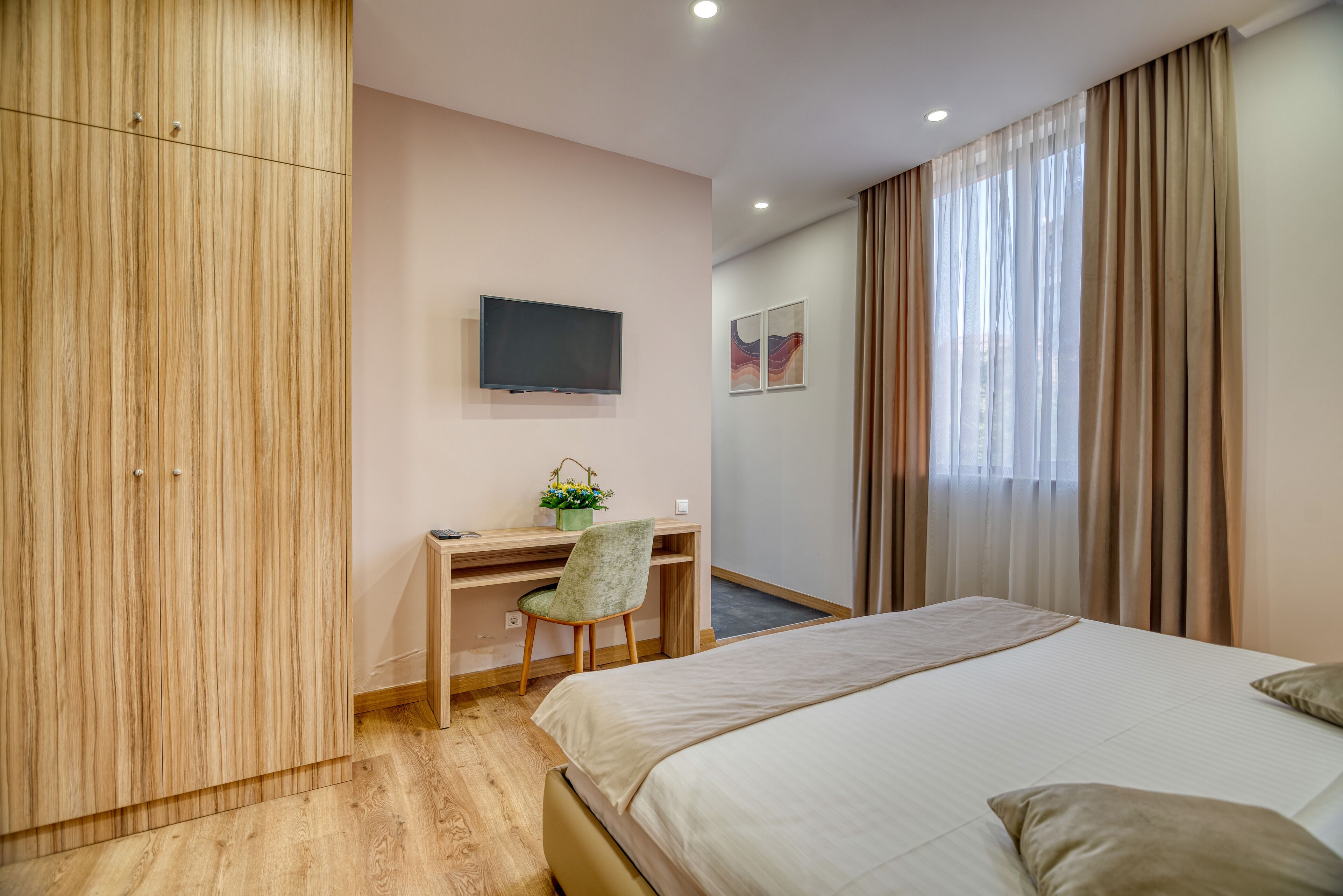 Una habitación de hotel con cama, un escritorio y una silla, televisor y ventana con cortinas.