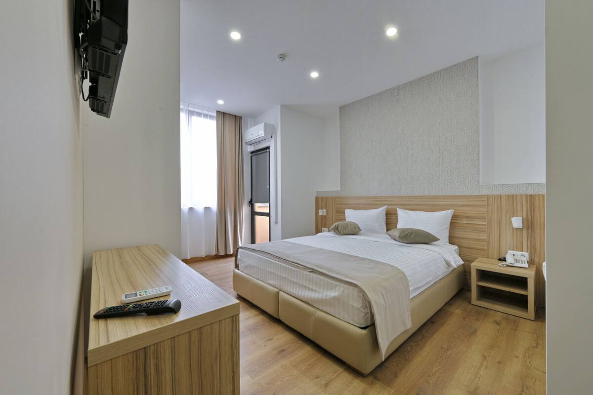 Una habitación de hotel con cama, mesita de noche y televisor montado en la pared.