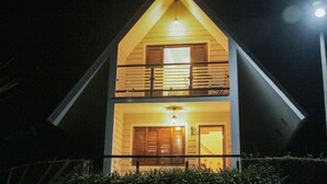 Una casa de dos plantas con un balcón en el piso superior, una entrada visible y una fuente de luz en la parte alta.