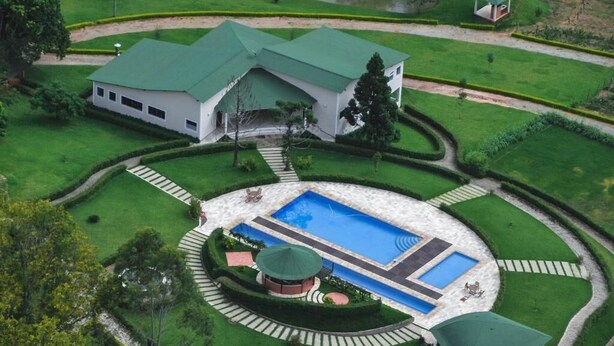 Una casa grande con piscina, rodeada de césped cuidado y un camino circular.