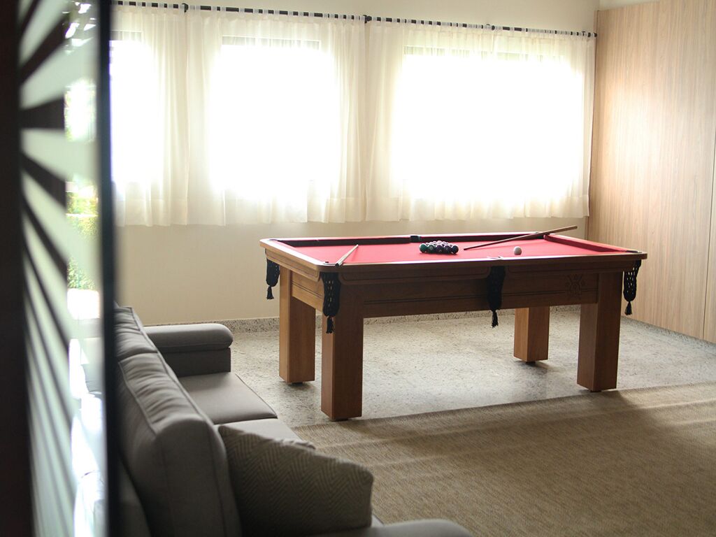 Una mesa de billar en una habitación con un sofá y una ventana con cortinas.