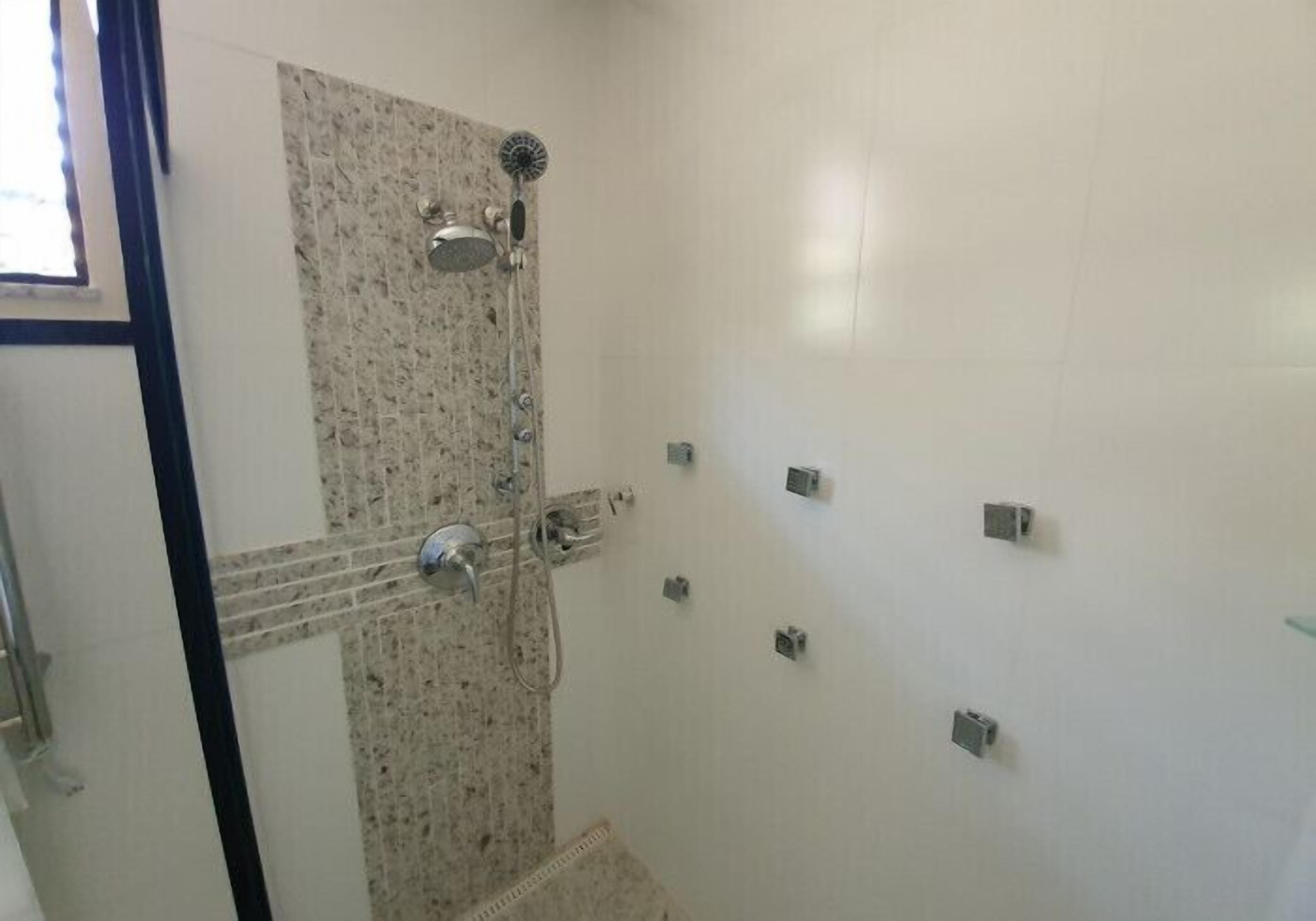 Una ducha con pared de baldosas de granito, cabezal de ducha de mano y grifo empotrado.