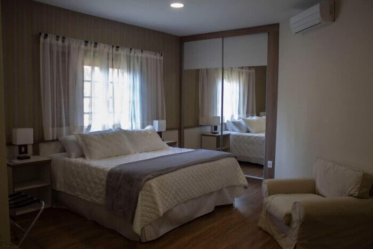 A hotel room with a large bed, a bedside table, a chair, and a mirror.