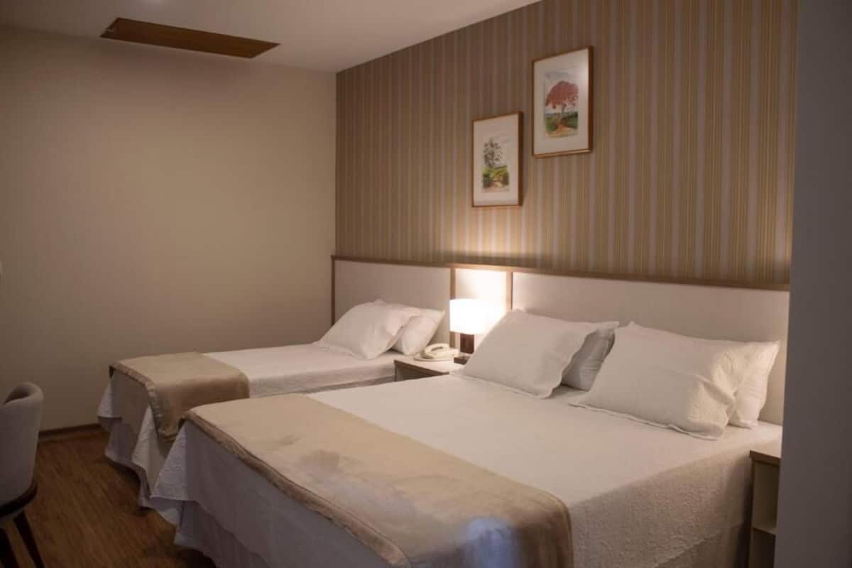 A hotel room with two beds, a bedside table with a lamp, and a chair.