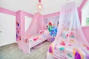A bedroom with two beds, pink walls, and Disney-themed decorations.