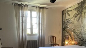 A bedroom with a bed, a desk, a chair, a radiator, and a large tropical mural on the wall. - Between golf and beach (Pléneuf-Val-André)