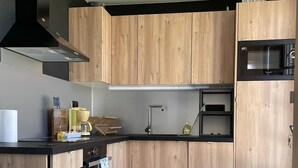 A modern kitchen with wooden cabinets, a black countertop, a built-in oven, and a microwave. - Between golf and beach (Pléneuf-Val-André)
