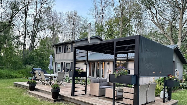 Una terraza moderna al aire libre con mobiliario de mimbre y macetas, conectada a una casa con ventanas amplias y un patio cubierto.