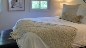 Un dormitorio con cama, ventana con persianas, lámpara y una obra de arte enmarcada en la pared.