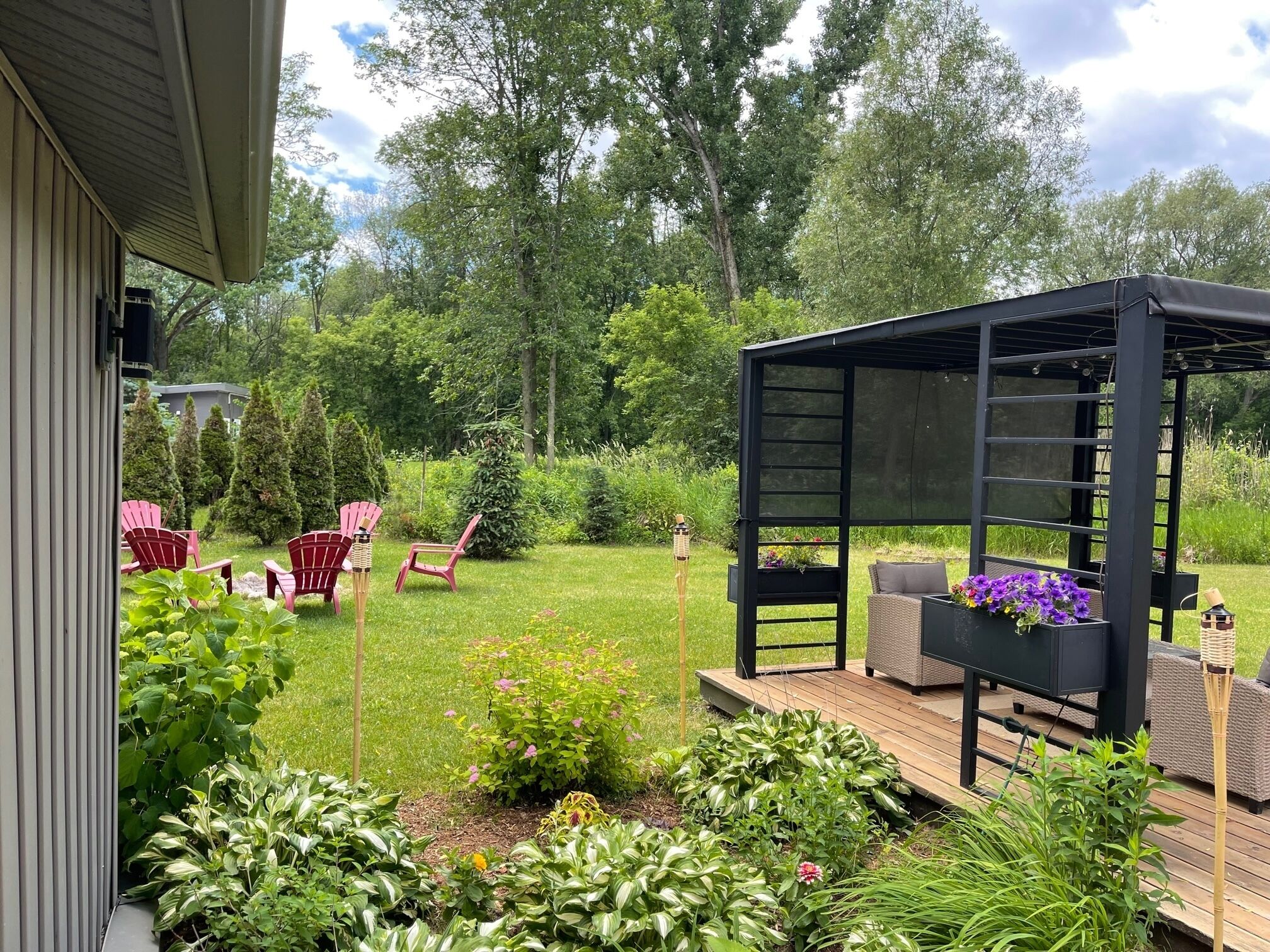 A deck with a pergola, outdoor seating, and a garden with various plants and flowers.
